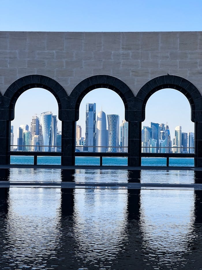 Stunning view of Doha's skyline through museum arches, reflecting on water.
